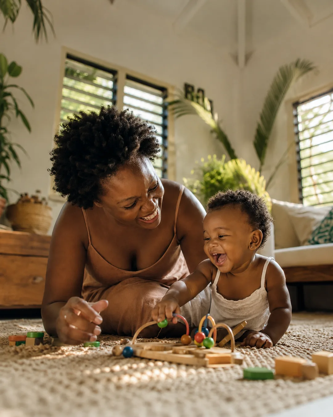 A caregiver playing with a happy toddler in a bright, sunlit Jamaican living room