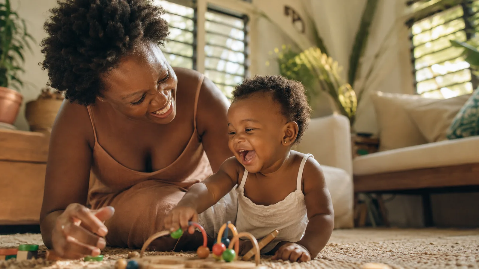 A caregiver playing with a happy toddler in a bright, sunlit Jamaican living room